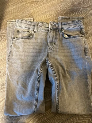 Gråa raka jeans med fem fickor - Snygga grå jeans med klassisk femficksmodell och raka ben. Jeansen har bälteshällor, knappgylf och en diskret patch bak i midjan. Tillverkade i mjukt denimtyg som ger en avslappnad look.
