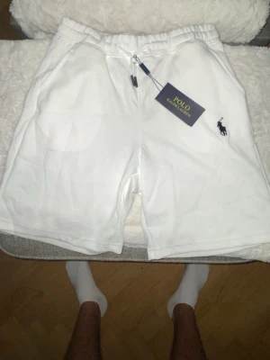 Vita shorts från Polo Ralph Lauren - Säljer ett par fräscha vita shorts från Polo Ralph Lauren med elastisk midja och snörning. Klassisk logga broderad i svart på vänster ben. Mjukt material som känns skönt mot huden och två sidofickor för enkel förvaring. Litet i storlek så passar både S och M. Helt nya aldrig använt 