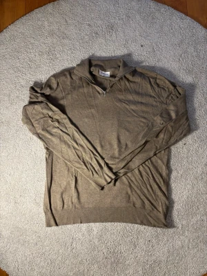 Beige halvzip tröja i bomull - Snygg beige långärmad tröja med halvzip och krage. Tillverkad i mjukt bomullsmaterial och har ribbade muddar vid ärmslut och nederkant. Perfekt för en avslappnad men ändå stilren look.