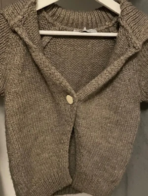 Beige stickad kofta från Zara - Kortärmad stickad kofta i beige från Zara med grovstickad struktur. Koftan har en stor krage, ribbade muddar och stängs med en stor, rund knapp framtill. Perfekt för lager på lager och en avslappnad men trendig look.