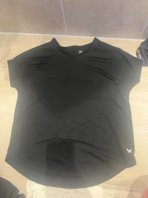 Svart tränings-tshirt från SOC - Säljer en svart tränings-tshirt från SOC i storlek XS. T-shirten har rund hals, korta ärmar och är tillverkad i ett tekniskt funktionsmaterial som håller dig torr och bekväm under träningen. Perfekt för gymmet eller löprundan.