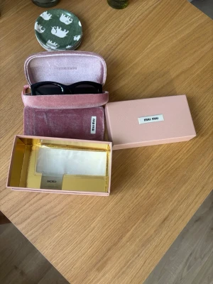 Svarta solglasögon från Miu Miu 09w - Stilrena svarta solglasögon från Miu Miu med bred båge och diskret gulddetalj vid skalmen. Kommer med original rosa sammetsfodral och putsduk. Perfekta för dig som vill ha en lyxig accessoar med statement-känsla.