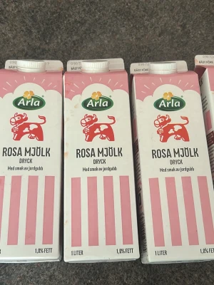 5 Arla Rosa Mjölk - bara förpackning  - En 1-liters förpackning Arla Rosa Mjölk Kartongen är rosa och vit med ränder och har en illustration av en rosa ko. Produkten är lågfett och har skruvkork på toppen.