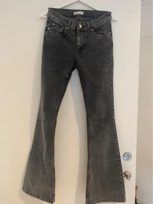 Grå bootcut jeans från Gina Tricot - Säljer ett par grå bootcut jeans från Gina Tricot med hög midja och utsvängda ben. Jeansen har klassisk femficksdesign och knappgylf. Perfekta för dig som gillar en retroinspirerad look och vill ha ett par snygga jeans med skön passform. Använd 1 gång