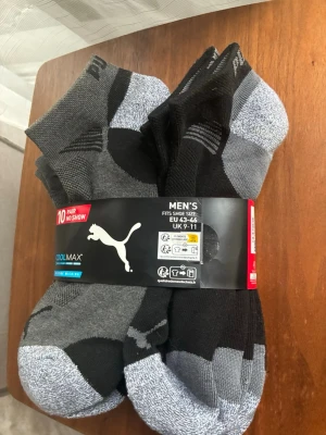 10-pack svarta och gråa Puma strumpor - Säljer ett 10-pack helt nya och oanvända svarta och gråa low cut strumpor från Puma. Strumporna har diskreta detaljer och logga, tillverkade i ett funktionsmaterial med Coolmax för extra komfort. Perfekta för sneakers och vardagsbruk.