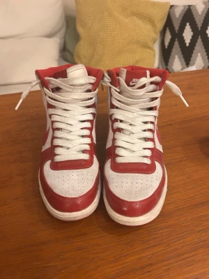 Nike Dunk High röd/vit sneakers - Nike Dunk High sneakers i rött och vitt med klassisk hög siluett. Skorna har vit bas med röda glansiga detaljer, perforerad tåbox och vita skosnören. Ovandelen är i läder och insidan är vadderad för extra komfort. Säljer då de är för stora, öppen för att diskutera pris💕