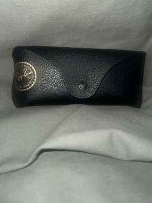 Svarta Ray-Ban Wayfarer solglasögon - Klassiska svarta Ray-Ban Wayfarer solglasögon med mörka glas. Säljs med original svart fodral i skinn och putsduk med Ray-Ban-logga. Snygg och tidlös modell som passar till allt.