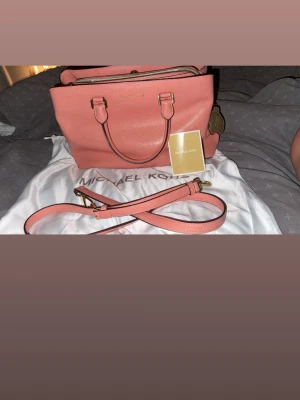 Michael Kors,Savannah,satchel leather,peach - Snygg korallrosa handväska från Michael Kors i strukturerat läder. Väskan har guldfärgade metalldetaljer, dubbla handtag och avtagbar axelrem. Klassisk fyrkantig form och dragkedja upptill. Perfekt för dig som vill ha en stilren och trendig accessoar.
