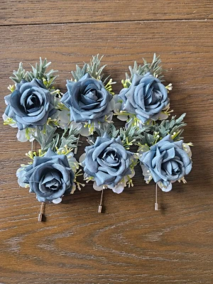 Blå/grön ros corsage med gröna blad - Säljer sex corsage med en stor blå konstgjord ros, omgiven av gröna blad och små vita samt gula detaljer. Perfekt som accessoar till kavaj, bal eller bröllop. Fästes enkelt med nål på baksidan. Ger en elegant och unik touch till din outfit.