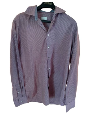 Rutig skjorta från Eton ”Contemporary fit” (43) - Klassisk långärmad skjorta från Eton med smått rutig mönster i mörkrött och vitt. Skjortan har knappar framtill, bred krage och är tillverkad i mjuk bomull. Perfekt för dig som gillar stilrena detaljer och tidlös design. I perfekt skick helt utan fläckar eller tecken på slitage. 