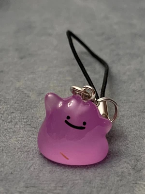Ditto charm Pokémon hänge nyckelring  - Jättegulligt hänge med en Ditto! Den är dessutom självlysande och lyser i mörkret.   OBS just denna berlocken har en tydlig repa på framsidan, därför säljer jag den till lägre pris.   Ditto-berlocken är ca 1,5 x 1,5 centimeter. Öglan är ca 5 cm lång.  Jättefin att sätta på din mobil, väskan eller i nycklarna exempelvis! Eller på ditt Switch eller 