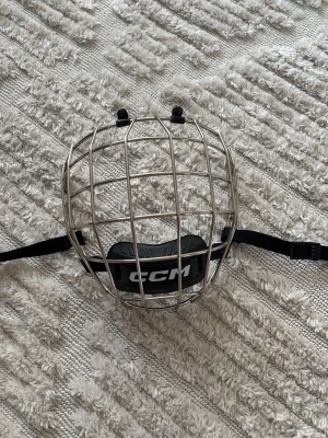 CCM hockeygaller i chrome storlek M - Säljer ett silverfärgat chrome hockeygaller från CCM med svart hakskydd och justerbara remmar. Gallret är tillverkat i metall och passar till hjälm för hockey eller liknande sporter. Perfekt för dig som vill ha extra skydd på isen och vill synas mycket. Endast använd två gånger. Nypris 750kr🥅😊