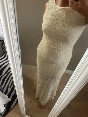 Ljus långklänning med struktur - Säljer en elegant ljus långklänning med strukturerat tyg och ärmlös design. Klänningen har en kroppsnära passform och rund halsringning. Perfekt för sommarens alla tillfällen. Märke och material är ej angivet.