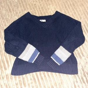 Mörkblå stickad tröja - Mörkblå stickad tröja från Hollister med v-ringning. Kortare i längd, fungerar bra som magtröja. 