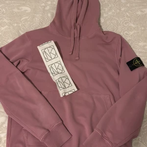 Rosa hoodie från Stone Island - Säljer en snygg rosa hoodie från Stone Island. Använd 3 gånger och är Absolut i topp skick!! Självklart äkta, köpt i NK Göteborg, Kvitto kommer med. Den har en klassisk design med en justerbar huva och en praktisk magficka. Perfekt för en avslappnad stil.   Kond: 10/10