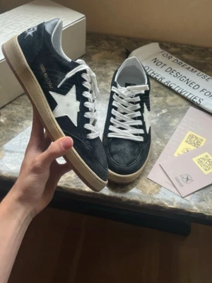 Golden Goose ballstar svart - Säljer nu dessa snygga golden goose ballstar i en snygg svart färg. Bekväma sneakers som är väldigt sköna nu under sommaren. Säljer pga att de inte kommer till speciellt mycket användning längre. Inte använda speciellt mycket och inga större synliga defekter på de. Storlek 43 TTS. Allt på bilderna är det som ingår vid köp.  Hör av er vid frågor! 
