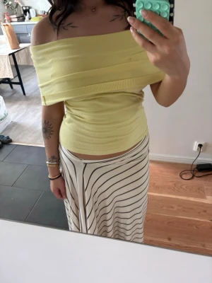 Ljusgul offshoulder topp - Trendig ljusgul offshoulder topp med ribbad struktur. Toppen är tight och har en bred kant som vilar över axlarna för en snygg och modern look. Perfekt för dig som vill ha en stilren och fräsch topp till sommaren.