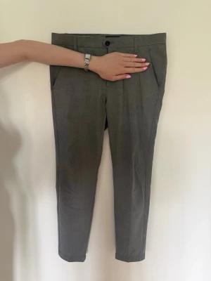 Grå kostymbyxor - Snygga grå kostymbyxor med slim passform och klassisk design. Byxorna har två sidofickor fram och två bakfickor med knapp. Perfekta för en clean och stilren look. Materialet känns mjukt och lätt.