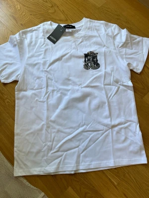 Vit Amiri t-shirt med ormtryck - Säljer en vit t-shirt från Amiri med ett svart ormtryck på bröstet och en stor orm tillsammans med Amiri-loggan på ryggen. Klassisk passform och rund hals. Perfekt för dig som vill ha en statement-tee med cool design.