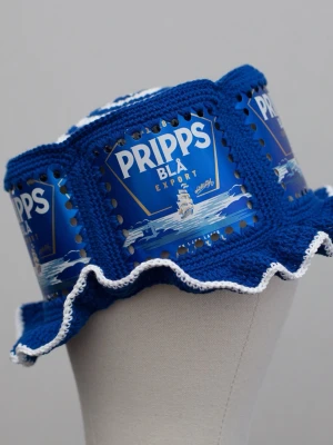 Virkad ölhatt Pripps blå - Unik virkad ölhatt med Pripps blå.   Virkad i 100% bomull. Passar upp till ca 60cm.  Vissa burkar kan ha mindre repor eller bucklor, vilket tyvärr kan uppstå under tillverkningen av hattarna. Insidan av burkarna slipas efter hålen tagits för att undvika vassa kanter. Därför kan det ibland finnas lite slipmärken, men det är inget som stör eftersom det är på insidan av hattarna.  Färger kan variera något beroende på skärminställningar.