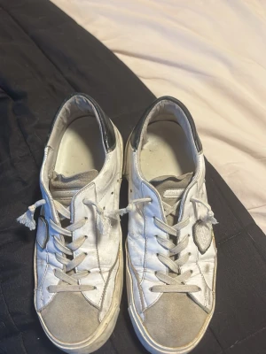 Philippe Model vita låga sneakers - Säljer ett par vita Philippe Model sneakers med grå detaljer och svart häl. Skorna har klassisk låg profil, vita snören och en ikonisk sköldlogga på sidan. Materialet är en mix av läder och mocka, vilket ger en schysst streetstil. Skicket är sådär, 4/10, men det ger dem ännu mer skön streetstil tycker jag, säljer för jag köpte ett par nya som passade bättre. Pris kan diskuteras vid snabb affär