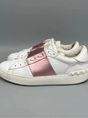 Valentino vita sneakers med rosa detalj - Snygga vita sneakers från Valentino med bred metallicrosa rem över mitten och nitar på hälen, första bilden är inte min men den andra 3 är mina, vill ni ha mer bilder så är de bara å skriva. Köptes för 5500, säljer för 2800 men pris kan diskuteras 