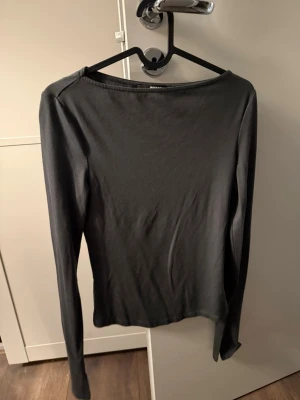 Mörkgrå långärmad topp från BikBok - En enkel och stilren mörkgrå långärmad topp från BikBok. Ärm med slit längst ner.  Modellen har en tight passform och boatneck rund halsringning. Perfekt att matcha med jeans eller kjol för en clean look.