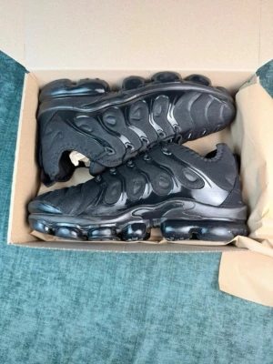 Nike Air Max Plus TN helsvarta sneakers - Säljer ett par helsvarta Nike Air Max Plus TN sneakers med ikonisk vågig design och synliga luftbubblor i sulan. Ovandelen är i mesh och syntet med plastdetaljer och klassisk Nike-logga på sidan. Grymt sköna och stilrena sneakers som passar till det mesta.