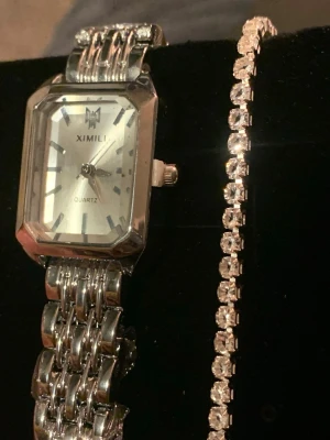 Silverfärgad Ximili klocka med länkarmband - Stilren klocka från Ximili med fyrkantig urtavla i silver och matchande länkarmband. Klockan har en klassisk design med tydliga markeringar och quartz-urverk. Perfekt accessoar för dig som gillar en elegant och tidlös look.