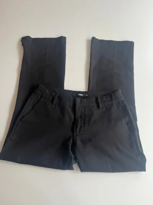 Svarta kostymbyxor från Bik Bok - Snygga svarta kostymbyxor från Bik Bok med utsvängd passform och pressveck. Byxorna har hällor för skärp, sidofickor och en bakficka. Tillverkade i ett mjukt och följsamt tyg som ger en clean look. De har även en slits på slutet av byxbenen. 