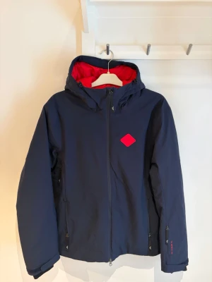 J.Lindeberg Ace Jacket TX Shell 2L - Skidjacka - Isolerad marinblå Skidjacka från J.Lindeberg i storlek L. Väldigt bra skick - knappt använd. - TX Shell 2L membran - Vatten och vindtät - Andningsförmåga - Snölås