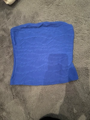 Blå strukturerad tubtopp - Säljer en blå tubtopp med snygg struktur i tyget. Toppen är axelbandslös och har en lätt stretchig känsla som gör att den sitter på plats. Perfekt att styla med jeans eller kjol för en trendig look.