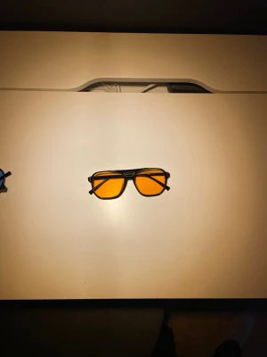 Svarta solglasögon med orangea glas - Coola solglasögon med svart ram och rektangulära orangea glas. Perfekt för dig som vill sticka ut och ge din stil en färgklick. Ramen är i syntetmaterial och glasen har en tydlig orange ton som ger ett unikt uttryck.