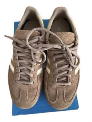 Bruna Adidas spezial! - Säljer ett par bruna Adidas Spezial sneakers i mocka med klassiska vita och guldiga stripes på sidan. Skorna har gummisula och lågt skaft, samt matchande bruna skosnören. Perfekta för dig som gillar retrostil och streetwear.❣️❣️