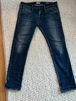 Blå slim fit jeans med dragkedjedetalj - Säljer ett par mörkblå slim fit jeans med snygga slitningar och kontrastsömmar. Jeansen har en unik dragkedjedetalj på bakfickan och coolt mönstrad söm. Perfekta för dig som gillar en modern och avslappnad stil.