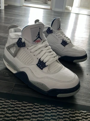 Air Jordan 4 White Midnight Navy - Säljer ett par Air Jordan 4 i färgen White Midnight Navy. Skorna har vit ovandel i läder, marinblå detaljer och gråa partier med svarta stänk. Klassisk mesh på sidorna och Jumpman-logga på plösen. Snygg retrostil och ikonisk siluett. Säljer de då står och samlar damm bara, använda endast ett fåtal gånger. Storlek 41 