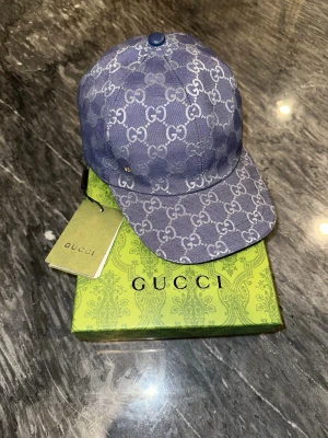 Blå Gucci Keps  - Snygg blå keps från Gucci. Kepsen har böjd skärm och justerbar baksida. Tillverkad i canvasmaterial och levereras med kartong och tagg. Perfekt för dig som vill sticka ut med en lyxig accessoar.