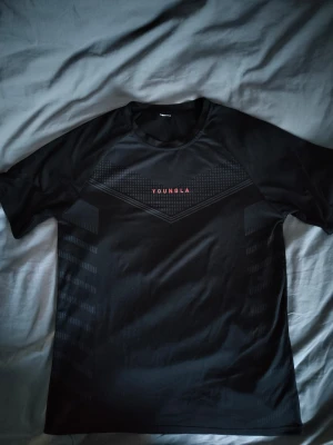 Svart tränings-tshirt från YOUNGLA - Träningströja i bra skick som endast är använd 2 gånger sen jag köpt den. Tillverkad i ett lätt och snabbtorkande material som passar perfekt för gym eller löpning. Bred: 50cm Längd: 60cm