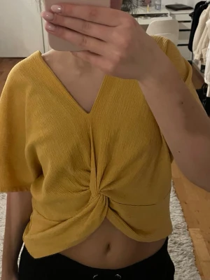 Gul topp  - Trendig gul croppad topp med v-ringning och twistad detalj framtill. Toppen har korta ärmar och är tillverkad i ett mjukt, ribbat material som ger en avslappnad men snygg look. Perfekt att styla med höga jeans eller kjol.
