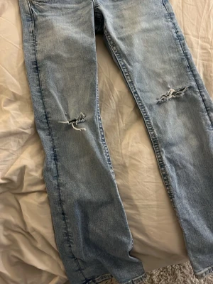 Ljusblå ripped jeans från Gina Tricot - Säljer ett par ljusblå jeans från Gina Tricot med slitna detaljer och hål på båda knäna. Klassisk femficksmodell med raka ben och snygg tvätt. Perfekta för en avslappnad och trendig look.