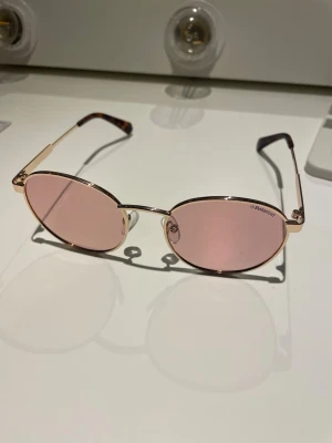 Polaroid ovala solglasögon rosa - Snygga solglasögon från Polaroid med tunna guldfärgade metallbågar och ovala rosa glas. Perfekt accessoar för att lyfta din stil med en trendig touch. Lätta och bekväma att bära, passar till många olika outfits. Jag skulle säga att de är för ett mindre huvud, altså mer för unga. Har aldrig använts. Pris kan diskuteras💕