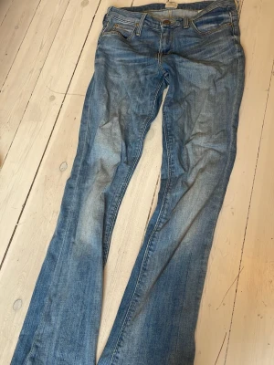 Blå raka jeans med låg midja - Snygga blå jeans med raka ben och låg midja. Klassisk femficksmodell med slitningar och ljusare partier framtill. Perfekta för en avslappnad och trendig look.