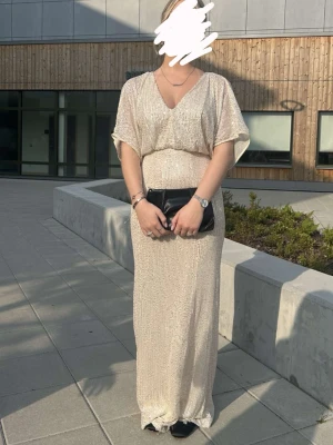 Lång glittrig champagneklänning - Elegant långklänning i champagnefärg med glittrigt tyg och v-ringad hals. Klänningen har korta ärmar och ett löst, bekvämt fall. Perfekt för speciella tillfällen där du vill glänsa lite extra. Skriv till mig för fler bilder❤️