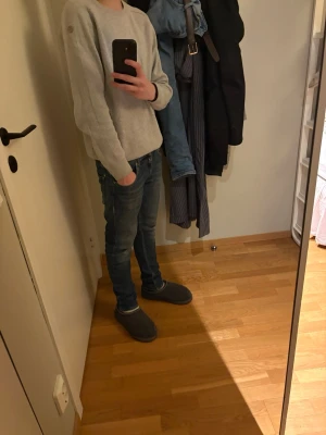 Ljusgrå tröja från Pelle P - Ljusgrå stickad tröja från Pelle P med rund halsringning och diskret logga på axeln. Tröjan har en klassisk passform och ribbade muddar vid ärmslut och nederkant. Perfekt för lager-på-lager och enkel att matcha med jeans.