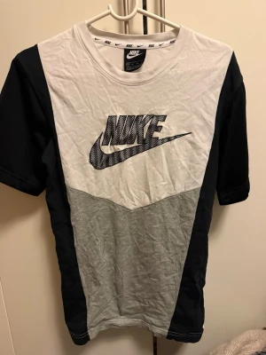 Nike t-shirt med logga, svart/vit/grå - Nike t-shirt i färgblock med svart, vit och grå. Stor Nike-logga framtill och klassisk rund halsringning. Tillverkad i mjuk bomull och har korta ärmar. Perfekt för en sportig och avslappnad stil.