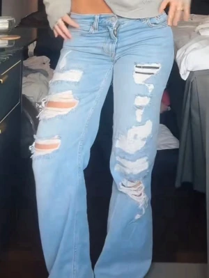 Ljusblå slitna jeans med hål - Säljer ett par ljusblå jeans med rejält slitna detaljer och stora hål på både lår och knän. Jeansen har en klassisk femficksmodell och rak passform. Perfekta för dig som gillar en edgy och avslappnad stil.