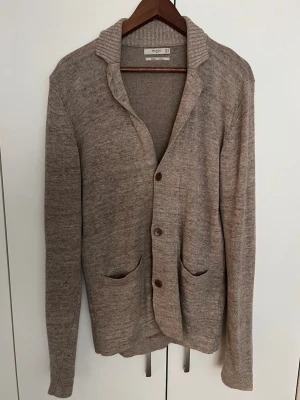 Beige kofta från Mango - Klassisk beige kofta från Mango i mjuk ullblandning. Koftan har två framfickor, ribbad krage och stängs med tre knappar framtill. Långärmad och perfekt för lager på lager under kyliga dagar.