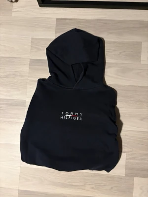 Svart hoodie med logga Tommy Hilfiger - Snygg svart hoodie från Tommy Hilfiger med klassisk logga tryckt på bröstet i vitt. Hoodien har en stor huva och en liten flaggdetalj på ärmen. Tillverkad i mjukt material som känns skönt mot huden. Hör av er om nu är intresserade eller har några frågor.✨