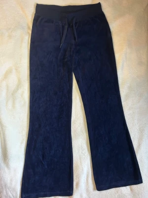 Marinblå velour mjukisbyxor från Gina Tricot - Marinblå mjukisbyxor i mjuk velour med utsvängda ben och bred resår i midjan med dragsko. Två bakfickor. 