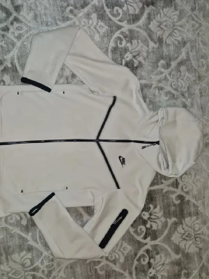 Nike tracksuit  - Snyggt beige loungewear set från Nike med hoodie och matchande byxor. Hoodien har svarta detaljer, dragkedja och fickor, samt Nike-logga på bröstet. Byxorna har resår i midjan, svarta snören och Nike-logga på benet. Perfekt för chill dagar hemma.